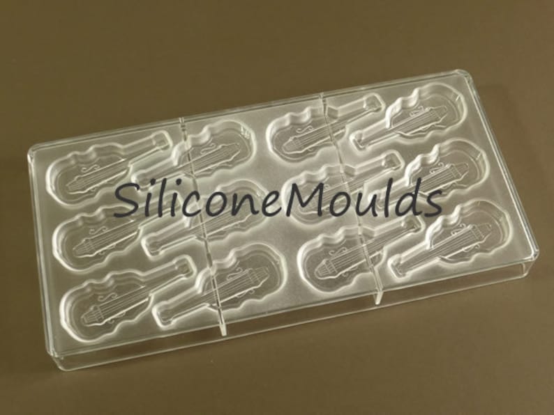 May include: Clear plastic mold with 9 cavities shaped like violins. The mold is designed for making chocolate or other edible treats.