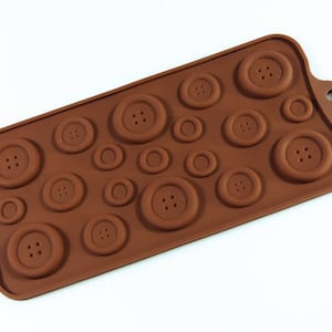 May include: Brown silicone mould with 16 button-shaped cavities. The mould is designed to create chocolate or candy buttons.