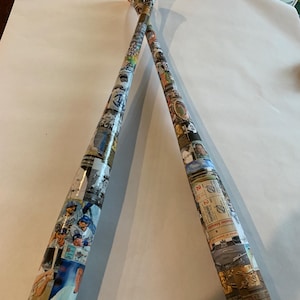 May include: Two wooden baseball bats covered in a collage of baseball photos and memorabilia. One bat has a blue end and the other has an orange end.