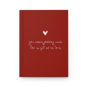 May include: A red journal with a white heart and the handwritten text, "you seem pretty sad for a girl so in love." The journal has a clean, minimalist design, perfect for writing or sketching.
