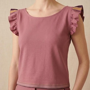 May include: A dusty rose-colored top featuring a wide scoop neckline and short flutter sleeves. The sleeves and the bottom hem are accented with a multi-colored striped trim in shades of yellow, purple, and brown, adding a subtle detail to the garment.