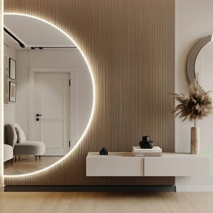 Può includere: Un corridoio moderno con un grande specchio rotondo circondato da un anello luminoso. Lo specchio è montato su una parete con pannelli di legno verticali. Uno scaffale a muro bianco con due cassetti è montato sotto lo specchio. Lo scaffale è decorato con un vaso nero, un piccolo oggetto nero e tre libri. Uno specchio rotondo piccolo è montato sulla parete a destra del grande specchio. Un vaso con erba secca è sullo scaffale sotto il piccolo specchio.