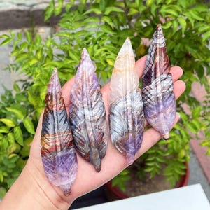 Peut inclure: Quatre plumes en pierre sculptée alignées, présentant chacune des motifs en bandes distincts dans des tons de violet, marron, blanc et orange translucide. Les pièces minérales polies affichent des variations de couleur naturelles.