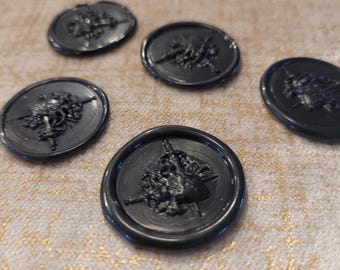 May include: A collection of five black wax seals with a detailed relief design. The seals are round and feature a classical bust with a crown. The seals are arranged on a textured, light-colored surface.