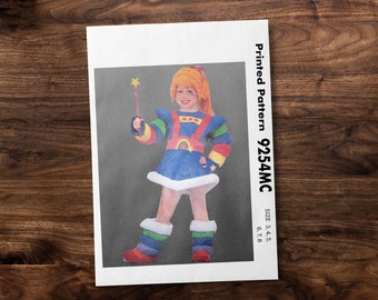 May include: A printed sewing pattern for a child's costume. The pattern is for a rainbow-colored dress with a star and rainbow design. The pattern is for sizes 3, 4, 5, 6, 7, and 8. The pattern number is 9254MC.