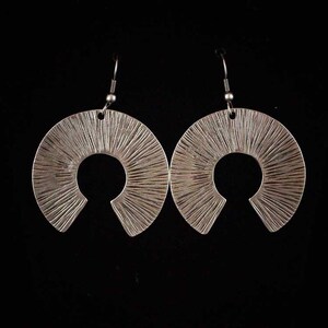 May include: A pair of silver earrings with a sunburst design. The earrings are made of metal and have a textured finish.