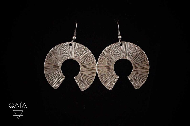 May include: A pair of silver earrings with a sunburst design. The earrings are made of metal and have a textured finish.