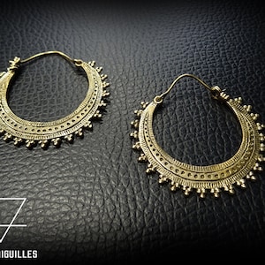 Peut inclure: Une paire de boucles d'oreilles créoles dorées avec des motifs complexes. Les boucles d'oreilles sont en métal et ont une forme circulaire avec une bordure décorative.