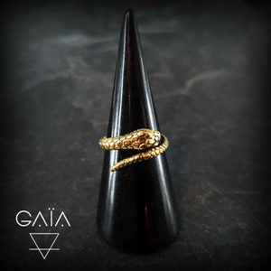Pode incluir: Um anel de cobra dourado em um suporte de anel preto. A cobra está enrolada ao redor do suporte do anel.