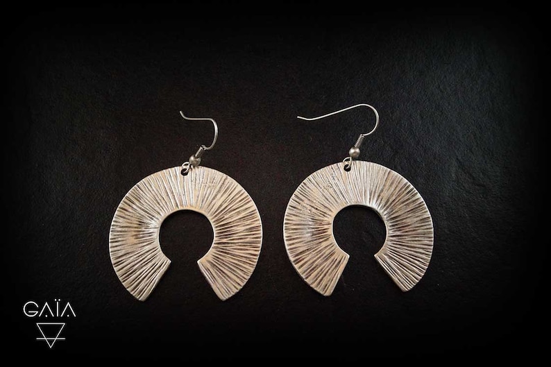 May include: A pair of silver hoop earrings with a textured, sunburst design. The earrings have a large, open circle shape.