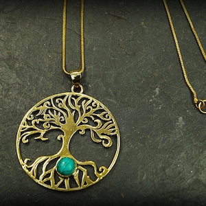May include: A gold necklace with a tree of life pendant featuring a turquoise stone. The pendant is intricately detailed with a tree and roots.
