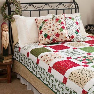 May include: A bed featuring a black metal headboard, a patchwork quilt with red, green, and cream holiday-themed fabric squares, and two decorative pillows. One pillow displays a Santa Claus pattern, while the other has a green and white holly print.