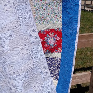 May include: A patchwork quilt featuring a variety of fabric patterns including a white and gray floral print, a cream background with small colorful flowers, a red floral section, and a dark blue floral print, all finished with a blue dotted border.