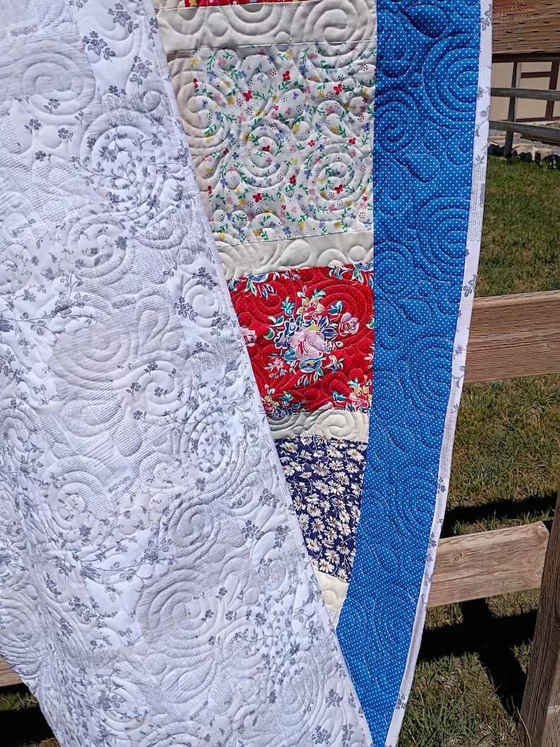May include: A patchwork quilt featuring a variety of fabric patterns including a white and gray floral print, a cream background with small colorful flowers, a red floral section, and a dark blue floral print, all finished with a blue dotted border.
