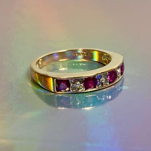 May include: A gold band ring with a row of red rubies and small diamonds set in the band.