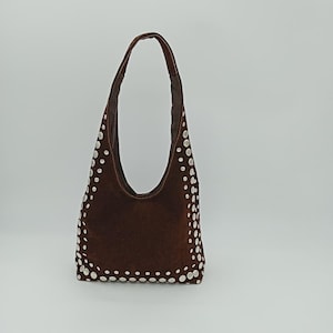 Può includere: Una borsa hobo in camoscio marrone con una sola tracolla. La borsa è decorata con borchie circolari bianche lungo i bordi. La borsa ha una forma curva e un interno marrone scuro.