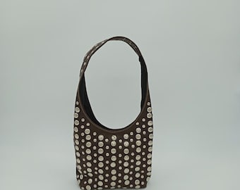 May include: A brown suede hobo bag with a single shoulder strap. The bag is covered in silver-colored studs. The interior of the bag is black.
