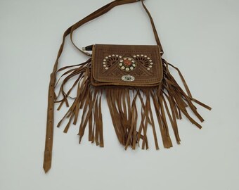 Può includere: Borsa a tracolla in pelle marrone con frange decorative e una lunga tracolla regolabile. La borsa presenta un design in rilievo sulla patta con un abbellimento centrale color gioiello e piccoli accenti di strass. Chiusura color argento.