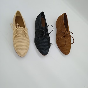 May include: Three lace-up shoes with a woven texture, arranged in a row. The shoes are colored beige, black, and brown. Each shoe features a pointed toe, a low heel, and matching laces tied at the top, showcasing a consistent design across all colors.