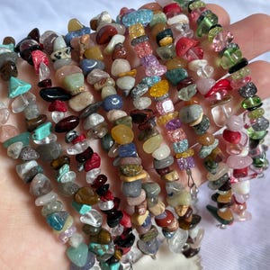 Pode incluir: Uma coleção de várias pulseiras feitas de fragmentos de pedras preciosas polidas em uma grande variedade de cores, incluindo vermelho, azul, verde, amarelo, rosa e transparente. Cada pulseira apresenta fragmentos de pedra irregulares.