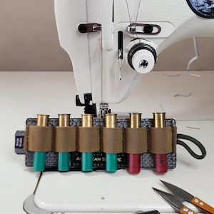 Puede incluir: Una máquina de coser con aguja e hilo, junto con un portacargadores con varios cartuchos. También hay un encendedor y unas tijeras pequeñas. La máquina tiene el texto "CAN S".