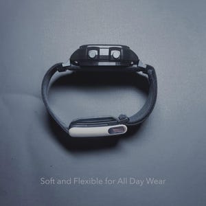 May include: Black digital watch with a gray fabric band. The watch face has two buttons and a display. The text "Soft and Flexible for All Day Wear" is at the bottom of the image.