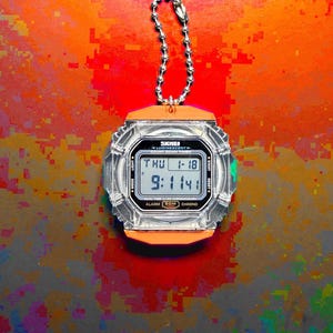 May include: A digital stopwatch with a clear, transparent plastic casing and orange accents. The face displays the text SKMEI, LUMINESCENT, COUNT DOWN TIMER, and shows the time 9:11:41 on Thursday, January 18. It includes a silver metal ball chain.