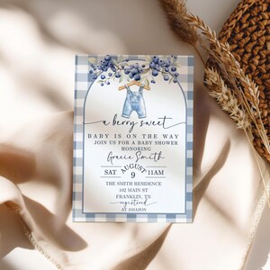May include: Baby shower invitation with a blue and white gingham border. The invitation features the text "a berry sweet" and "Baby is on the way". It includes details for Gracie Smith's baby shower, including the date, time, and location.