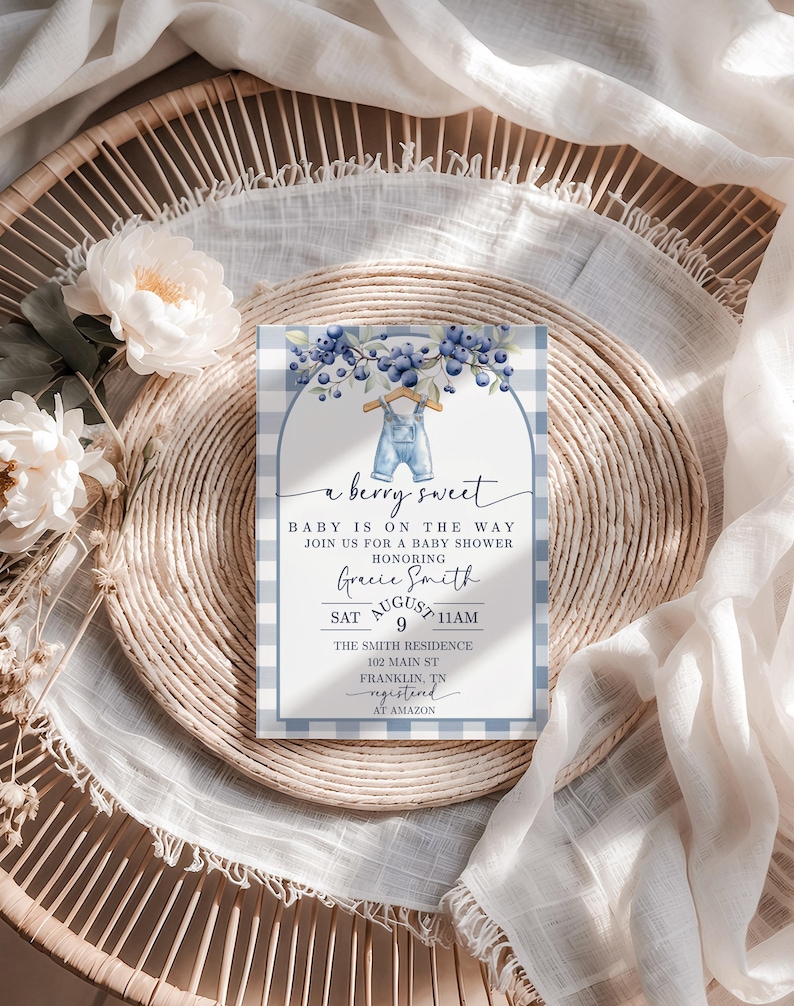 May include: A baby shower invitation with a blue and white gingham pattern. The invitation features the text "a berry sweet" and details for the event, including the date, time, and location. The design includes blueberries and a pair of overalls.