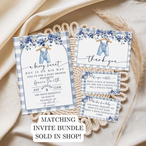 May include: A baby shower invitation suite with a blueberry theme. The invitation features a blue gingham pattern, blueberry sprigs, and a pair of overalls. The text reads "a berry sweet boy is on his way". Includes thank you and raffle cards.