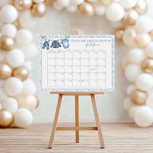 May include: A baby shower calendar on a wooden easel. The calendar is decorated with blue watercolor illustrations of baby clothes and the text "Guess the Arrival Date of Baby Brown." The calendar is surrounded by white and gold balloons.