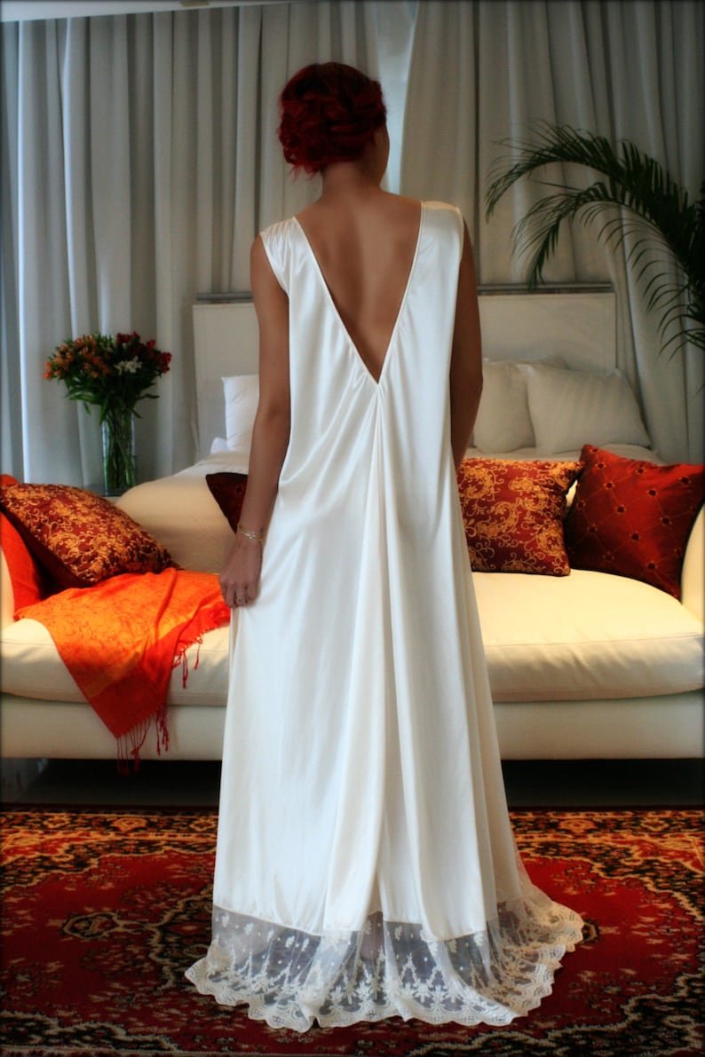 May include: A white satin slip dress with a deep V-neckline and lace trim. The dress is worn by a person with red hair and is photographed against a white background.