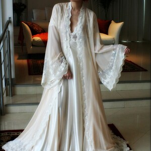 May include: A white satin and lace robe with long sleeves and a V-neckline. The robe has a delicate lace trim and a flowing silhouette.