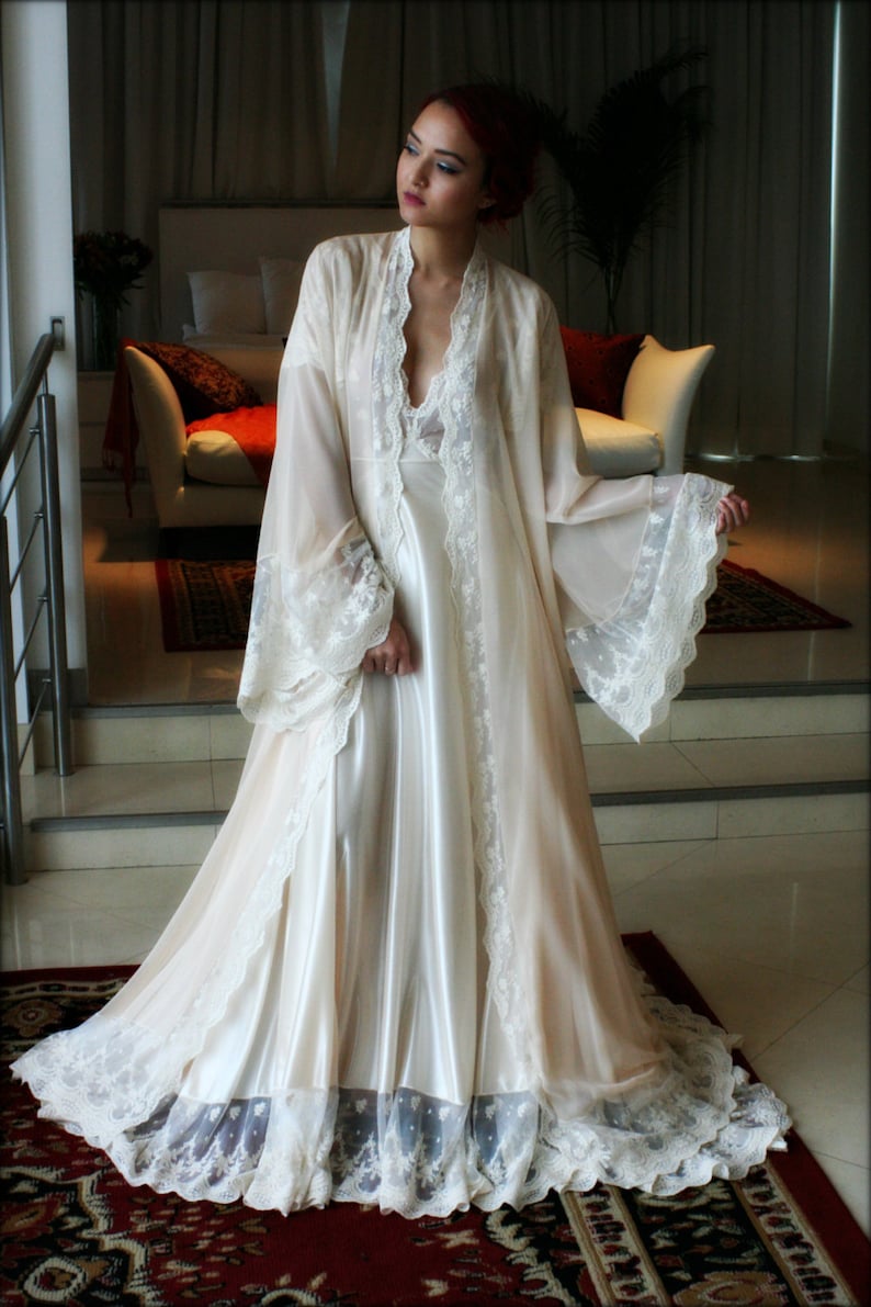 May include: A white satin and lace robe with long sleeves and a V-neckline. The robe has a delicate lace trim and a flowing silhouette.