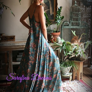 Puede incluir: Vestido largo de color turquesa con un estampado floral de flores rosas y p&aacute;jaros. El vestido tiene tirantes finos y un dise&ntilde;o largo y fluido. El texto "Sarafina Dreams" es visible en la imagen.