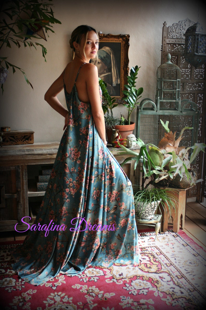 Puede incluir: Vestido largo de color turquesa con un estampado floral de flores rosas y p&aacute;jaros. El vestido tiene tirantes finos y un dise&ntilde;o largo y fluido. El texto "Sarafina Dreams" es visible en la imagen.