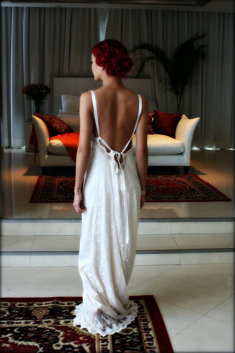 Puede incluir: Una mujer con el pelo rojo lleva un vestido blanco de encaje con la espalda descubierta. El vestido tiene una cinta blanca atada en la espalda.