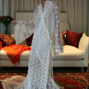 May include: A white lace robe with long sleeves and a flowing skirt. The robe is decorated with delicate floral embroidery.