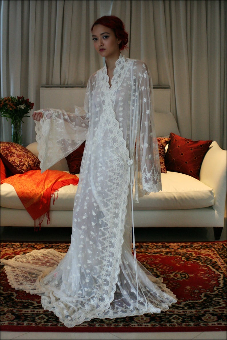 May include: A white lace robe with long sleeves and a flowing skirt. The robe is decorated with delicate floral embroidery.