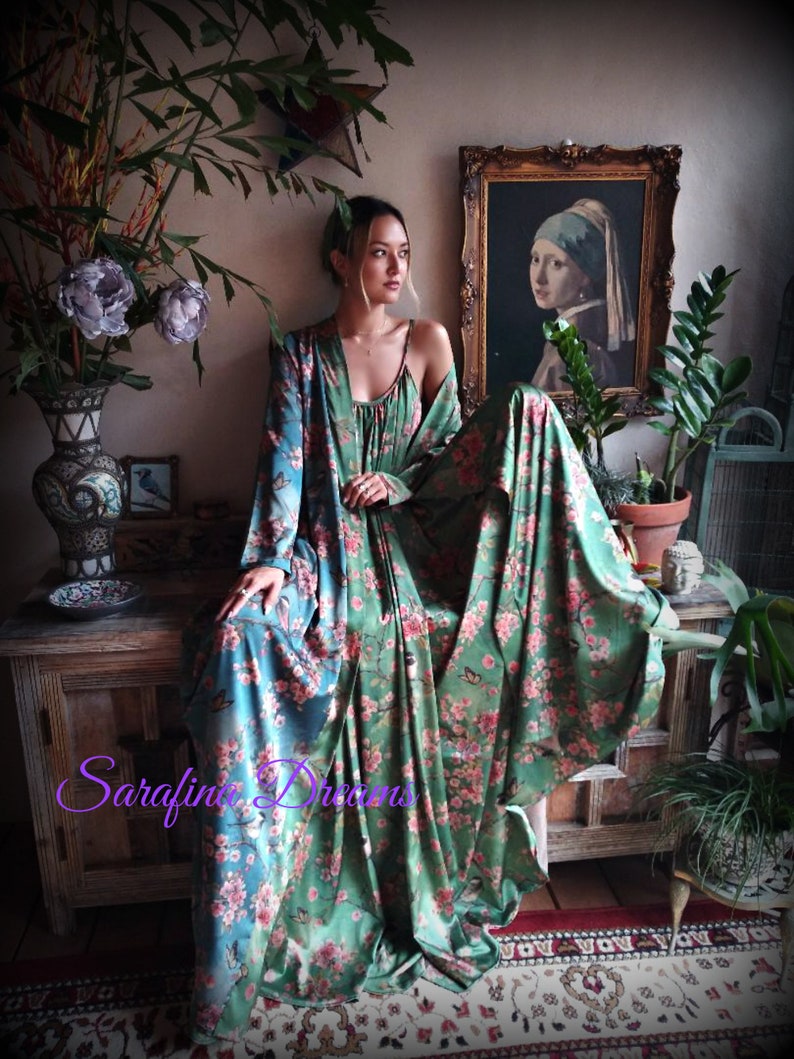 Puede incluir: Un vestido largo con estampado floral y una bata a juego en tonos verde y turquesa. El vestido presenta un delicado estampado floral rosa y detalles de mariposas. La imagen incluye el texto "Sarafina Dreams" en cursiva.