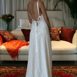 Puede incluir: Un vestido de novia de encaje blanco con la espalda baja y un lazo de cinta de sat&eacute;n. El vestido es fluido y tiene un delicado encaje.