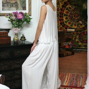 May include: A two-piece white outfit consisting of a sleeveless, loose-fitting top with a scoop neckline and matching wide-leg trousers. The ensemble is made of a lightweight, solid white fabric that drapes loosely, creating a relaxed silhouette.