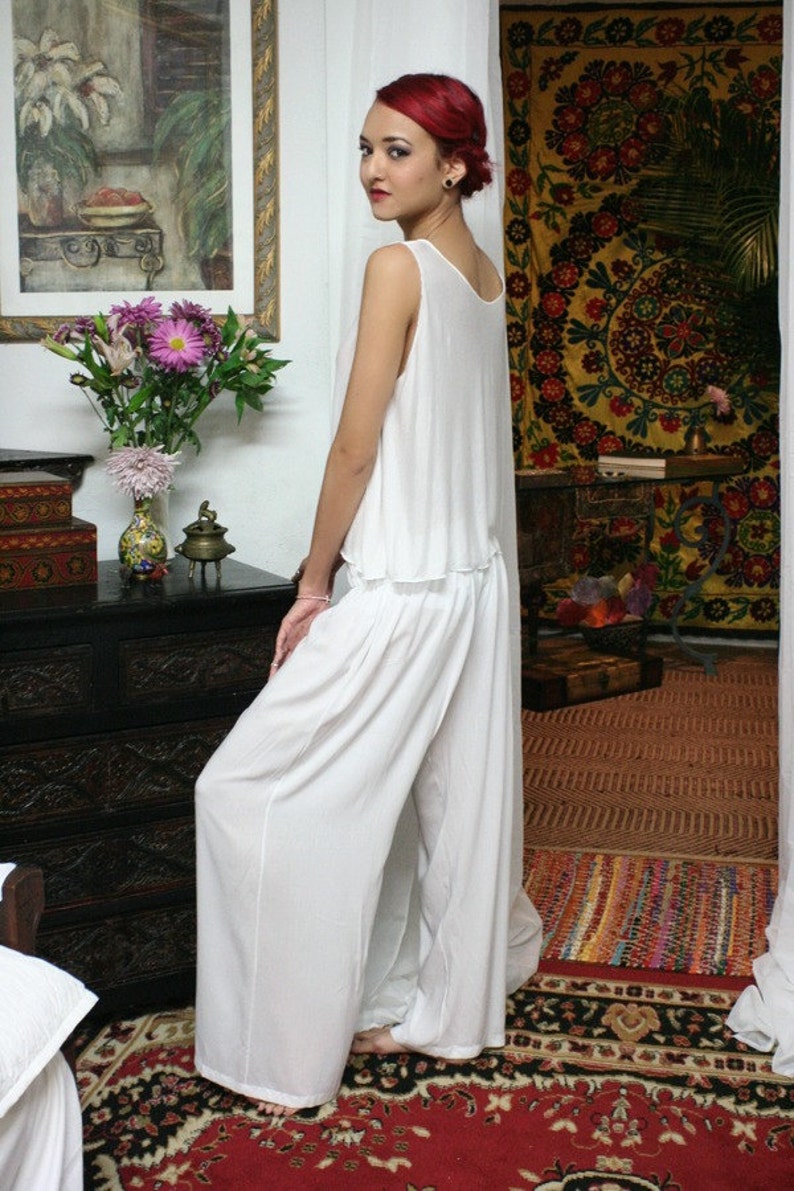 May include: A two-piece white outfit consisting of a sleeveless, loose-fitting top with a scoop neckline and matching wide-leg trousers. The ensemble is made of a lightweight, solid white fabric that drapes loosely, creating a relaxed silhouette.