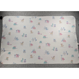 May include: A rectangular, off-white baby blanket with a repeating pattern of colorful cartoon animals. The illustrations include bears, horses, and figures in pink, blue, and green. The blanket is made of a soft material.