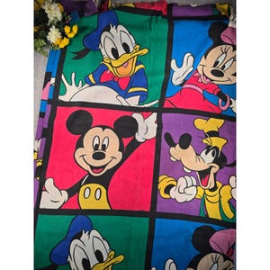 May include: A colorful fabric featuring a grid pattern with illustrations of Disney characters including Donald Duck, Minnie Mouse, Mickey Mouse, and Goofy. Each character is set within a distinct colored square, showcasing vibrant hues of red, blue, green, and purple.