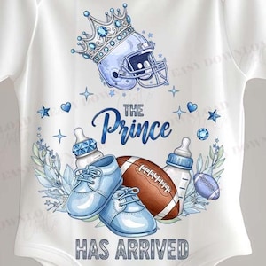 May include: White baby onesie with a blue and brown graphic. The design includes a football helmet, crown, baby shoes, a football, and the text "The Prince Has Arrived". The design is in shades of blue and brown.