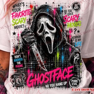 May include: A white t-shirt featuring a graphic of the Ghostface character in a hooded robe holding a knife. The design includes neon-colored paint splatters, grid lines, and text such as "What's your favorite scary movie?", "Don't answer the phone", and "Ghostface".