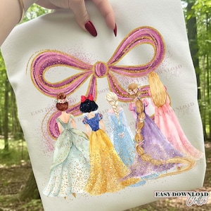 Puede incluir: Una sudadera de color claro con una ilustración de acuarela de cinco princesas. Las princesas están representadas de espaldas, con vestidos y peinados coloridos. Un gran lazo rosa con detalles de purpurina dorada está encima de ellas. El texto "EASY DOWNLOAD Crafts" es visible.