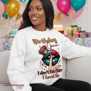 May include: White sweatshirt with a graphic design featuring the text "Birthday Queen" in gold glitter lettering. The design includes a crown, lips with a leopard print, and the phrase "I don't Get Older I Level Up."