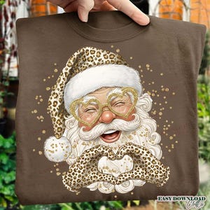 May include: Brown sweatshirt featuring a Santa Claus design. Santa wears heart-shaped glasses and a leopard print hat and gloves forming a heart. The design includes gold glitter accents and the text "EASY DOWNLOAD Crafts".